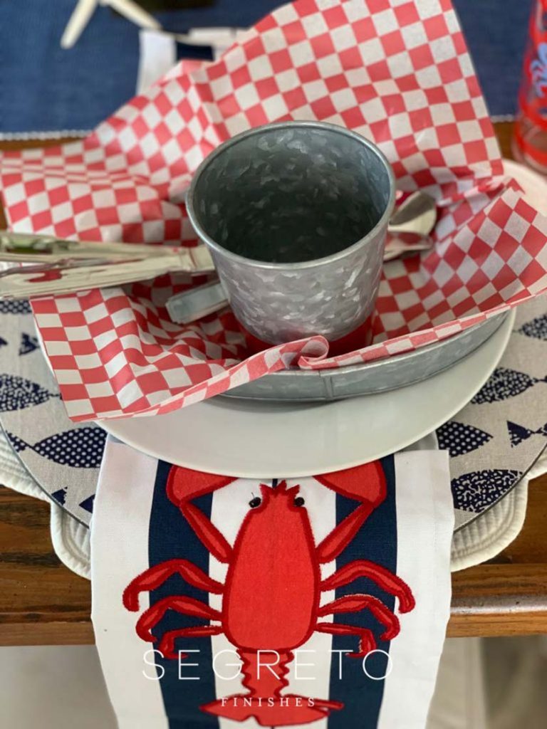 cup & silverware in paper napkin within bowl over lobster towel